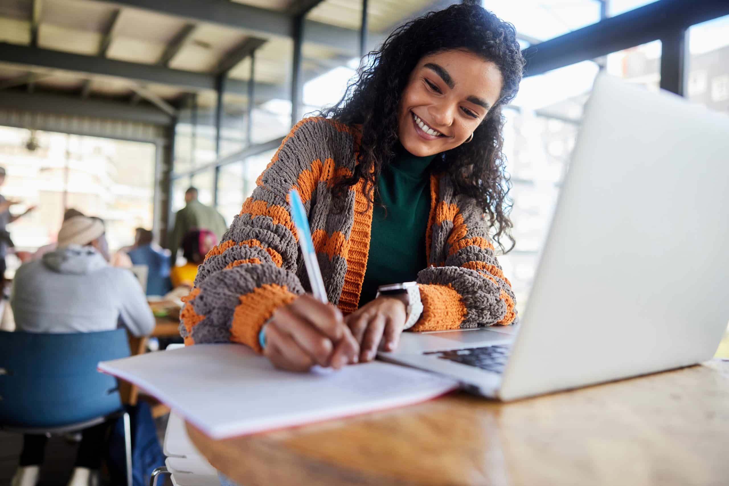 Young female college student smiling while doing homework in a school cafeteria